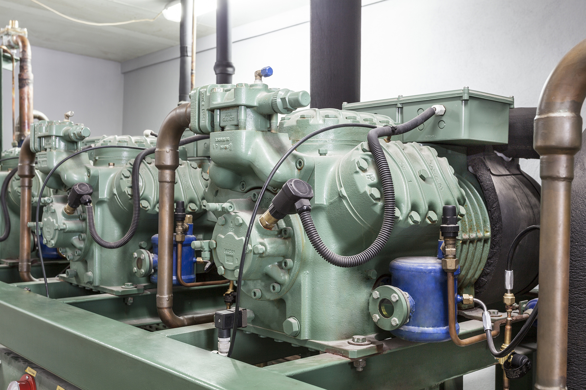 A large commercial three-stage reciprocating chiller installed within a mechanical plant room, servicing a commercial building HVAC system in Australia. The chiller features multiple reciprocating compressors, chilled water pipework, isolation valves, pressure gauges, control panels, and industrial mechanical services infrastructure designed for reliable cooling performance in medium to large commercial facilities. The image highlights critical fixed assets commonly found in commercial office buildings, hospitals, shopping centres, and industrial facilities across Sydney, Melbourne, and Canberra. The scene represents commercial HVAC engineering, preventative maintenance, energy management, plant reliability, and lifecycle management of major mechanical services equipment.