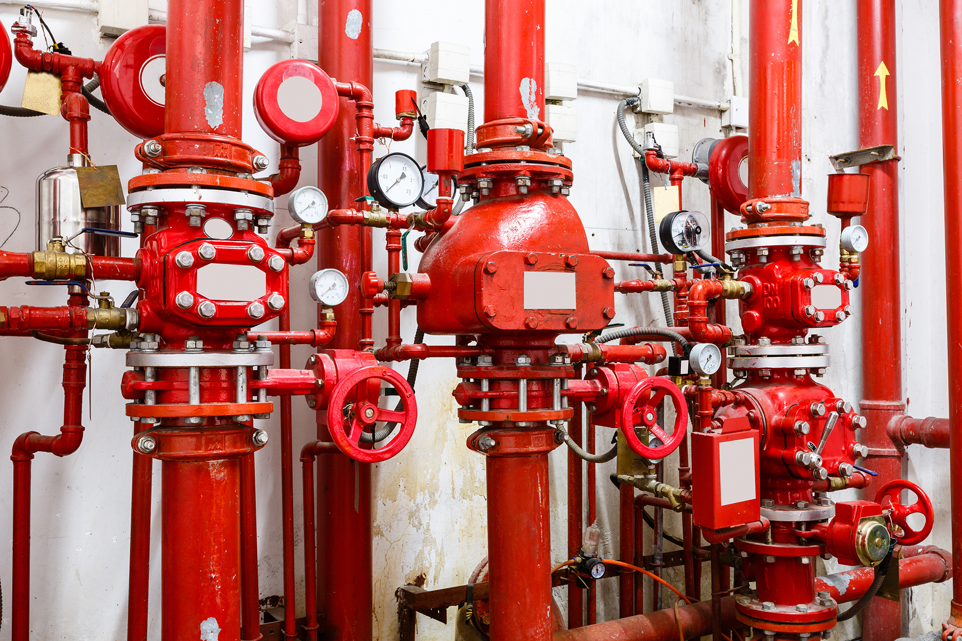 Complex fire sprinkler system in a commercial building fire control room featuring sprinkler alarm valves, pumps, pipework, isolation valves, gauges, and compliance signage, highlighting the importance of detailed fire asset registers.