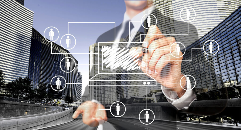 xecutive standing in front of four commercial city buildings, drawing a building diagram on a glass board with connected stakeholder icons, representing commercial property asset registers, building data management, and asset lifecycle planning.