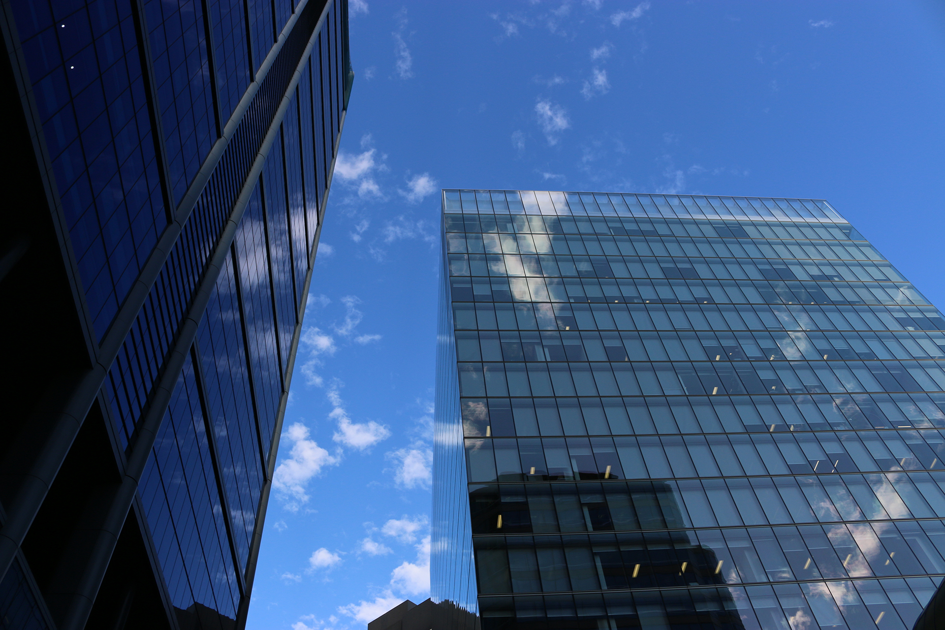 Two modern commercial office towers on Melbourne's St Kilda Road with reflective mirror-glass facades, viewed from street level looking upward between the buildings, showcasing unsupervised building management and facility management services.