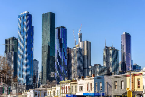 Melbourne city skyline in Victoria, Australia, featuring modern skyscrapers and buildings under construction rising above older North Melbourne buildings under a clear blue sky.