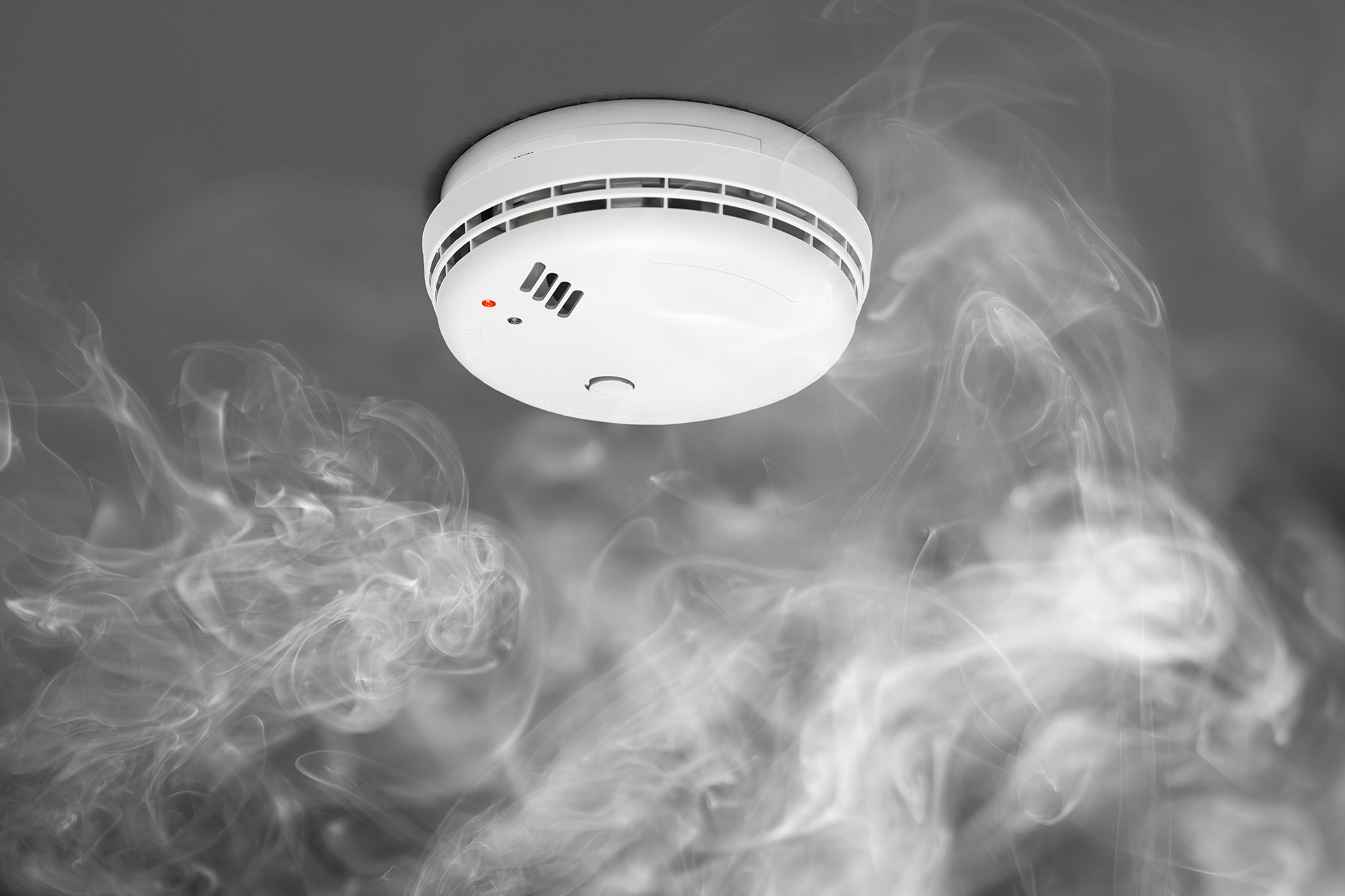 Ceiling-mounted smoke detector surrounded by dense smoke, demonstrating the importance of early fire detection systems in commercial and residential buildings.