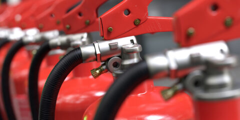 Close-up view of a row of commercial fire extinguishers aligned in sequence, highlighting fire safety equipment and compliance requirements for buildings in Sydney, Melbourne and Canberra.