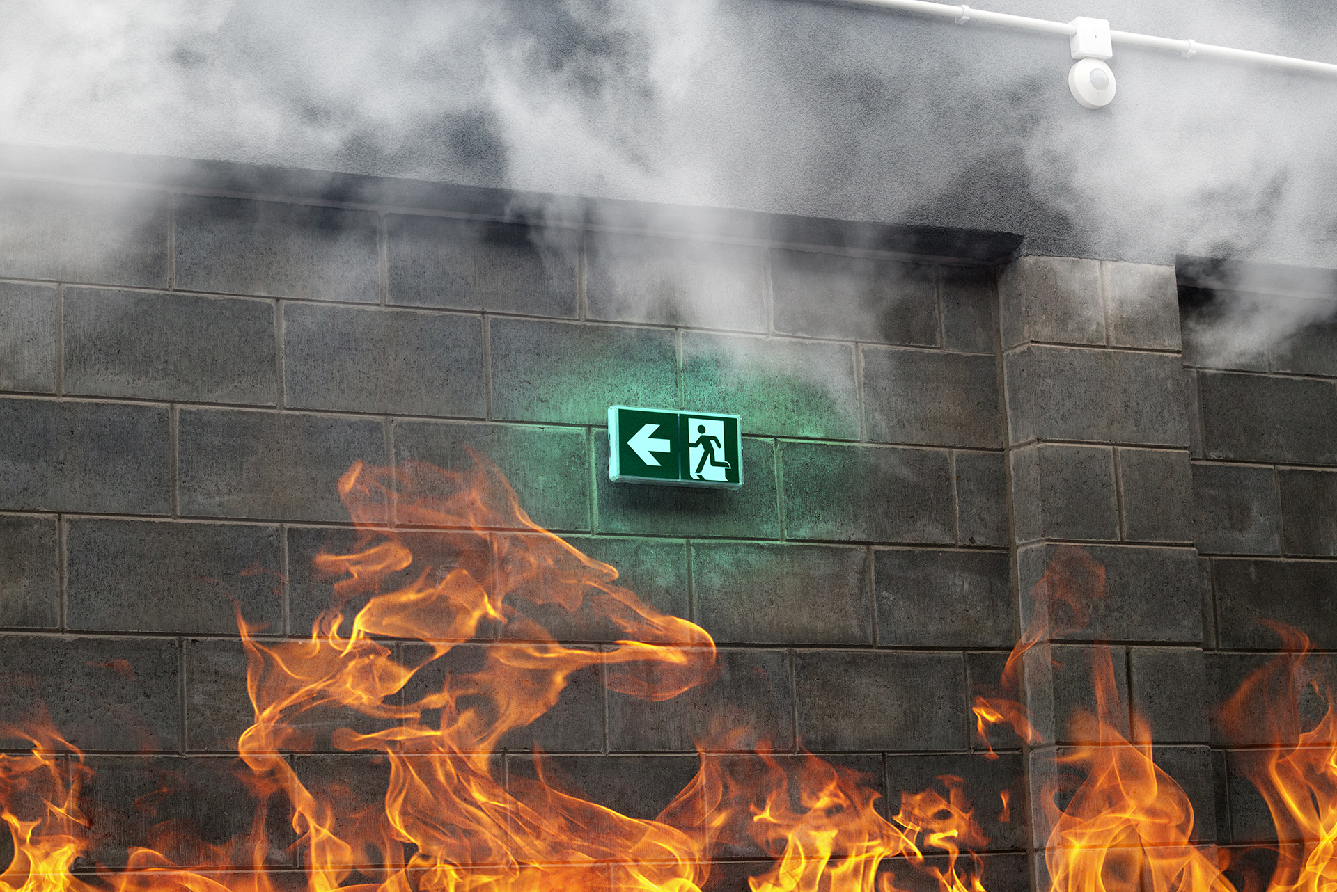 Emergency exit sign mounted on a brick wall surrounded by smoke and visible flames, highlighting the importance of emergency egress systems and fire safety compliance in commercial buildings.
