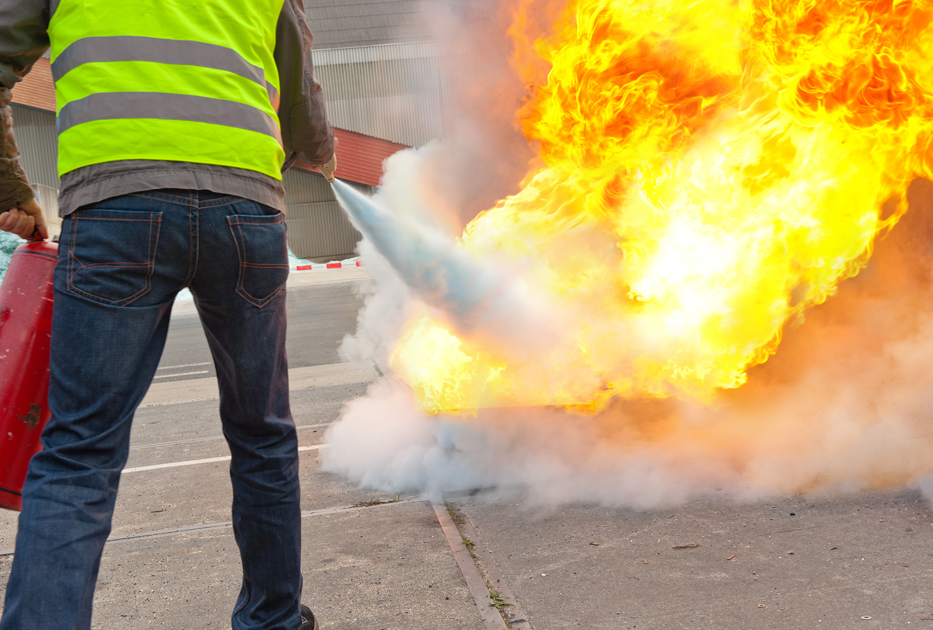 Fire safety instructor demonstrating the correct use of a portable fire extinguisher to extinguish a fire with large flames during emergency response training.
