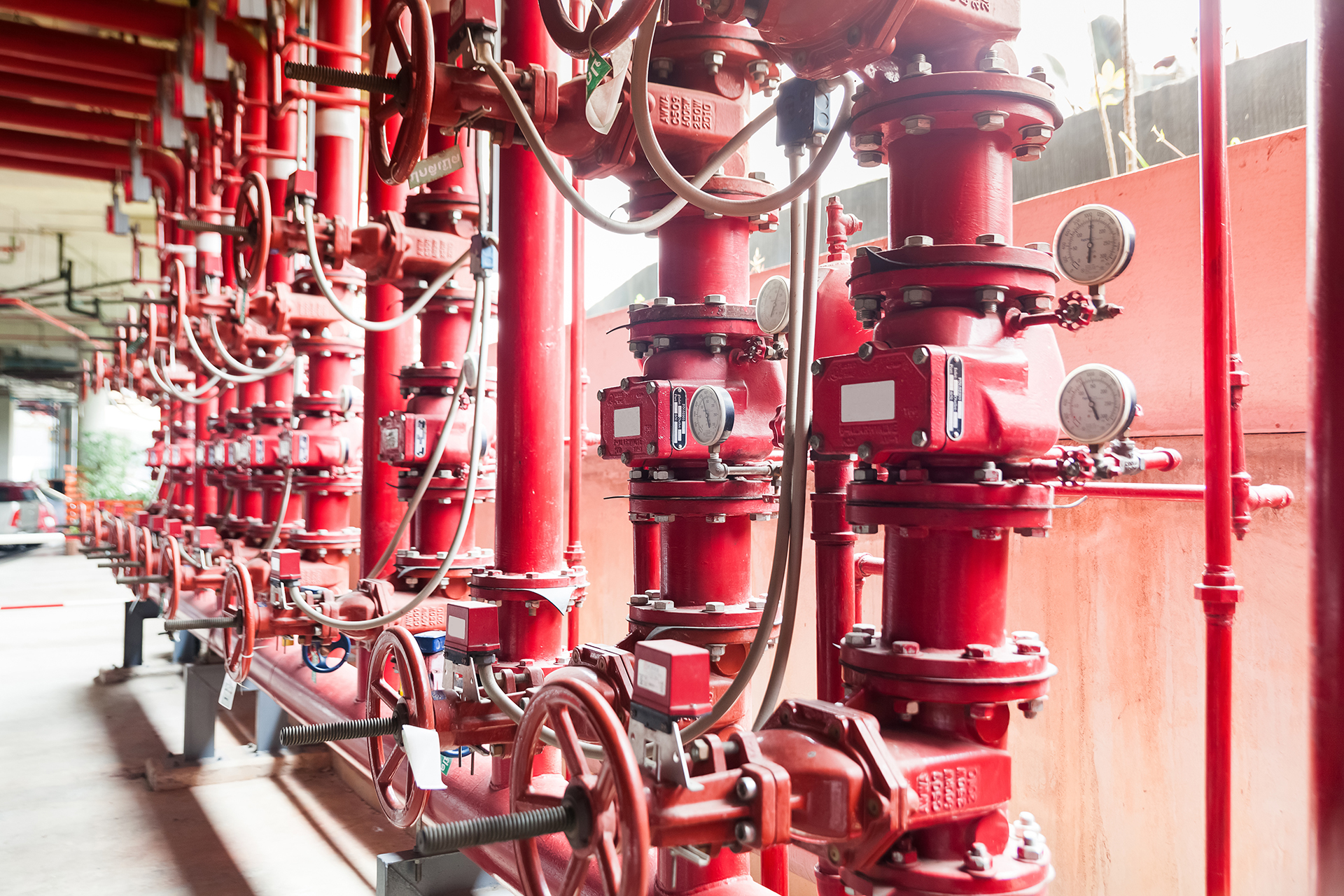 Commercial fire sprinkler alarm valve set featuring alarm valves, gate valves, fire pumps, pipework and associated fire protection equipment within a building fire services room.