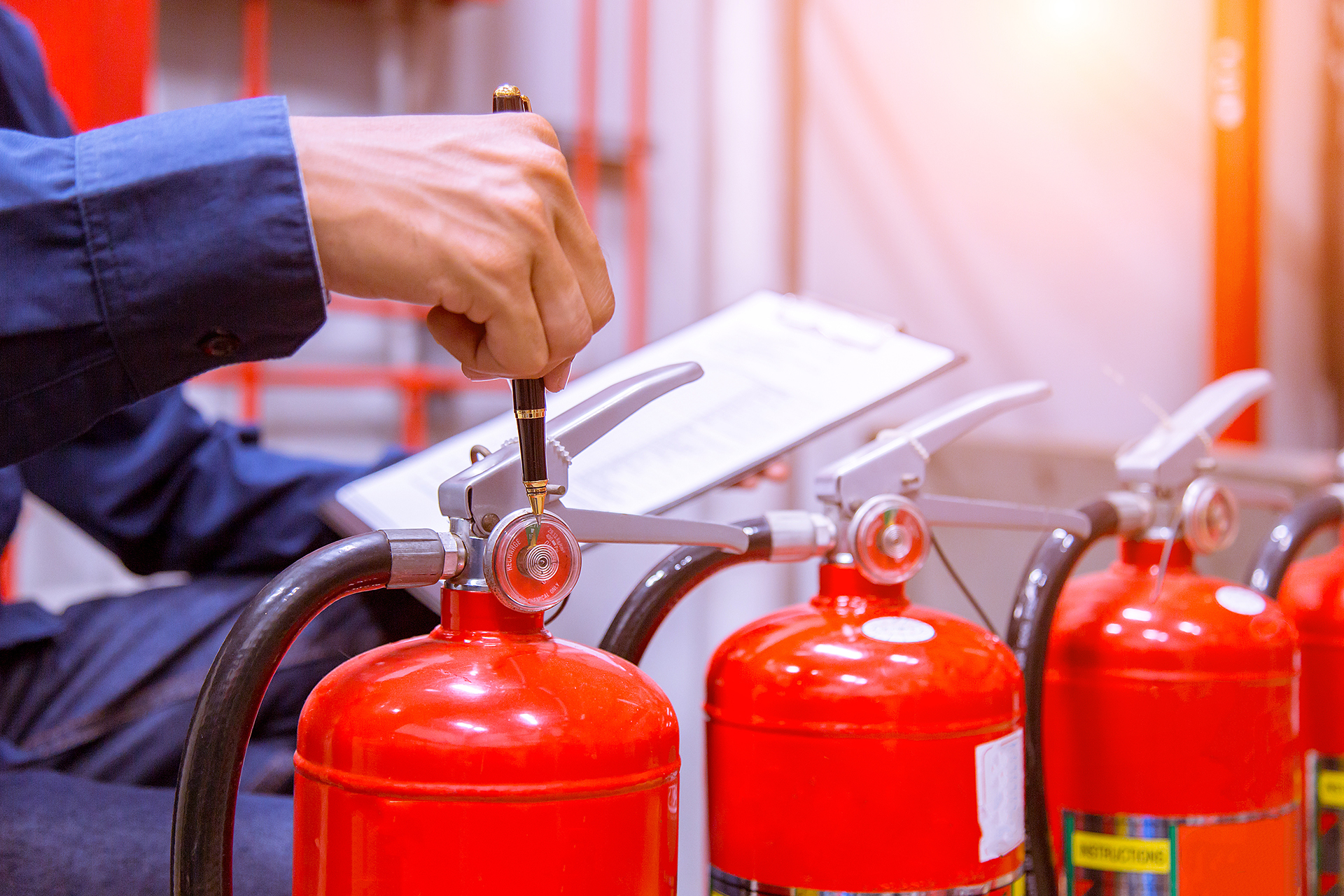 Fire protection technician carrying out a compliance inspection of portable fire extinguishers in a modern office building and recording maintenance observations.