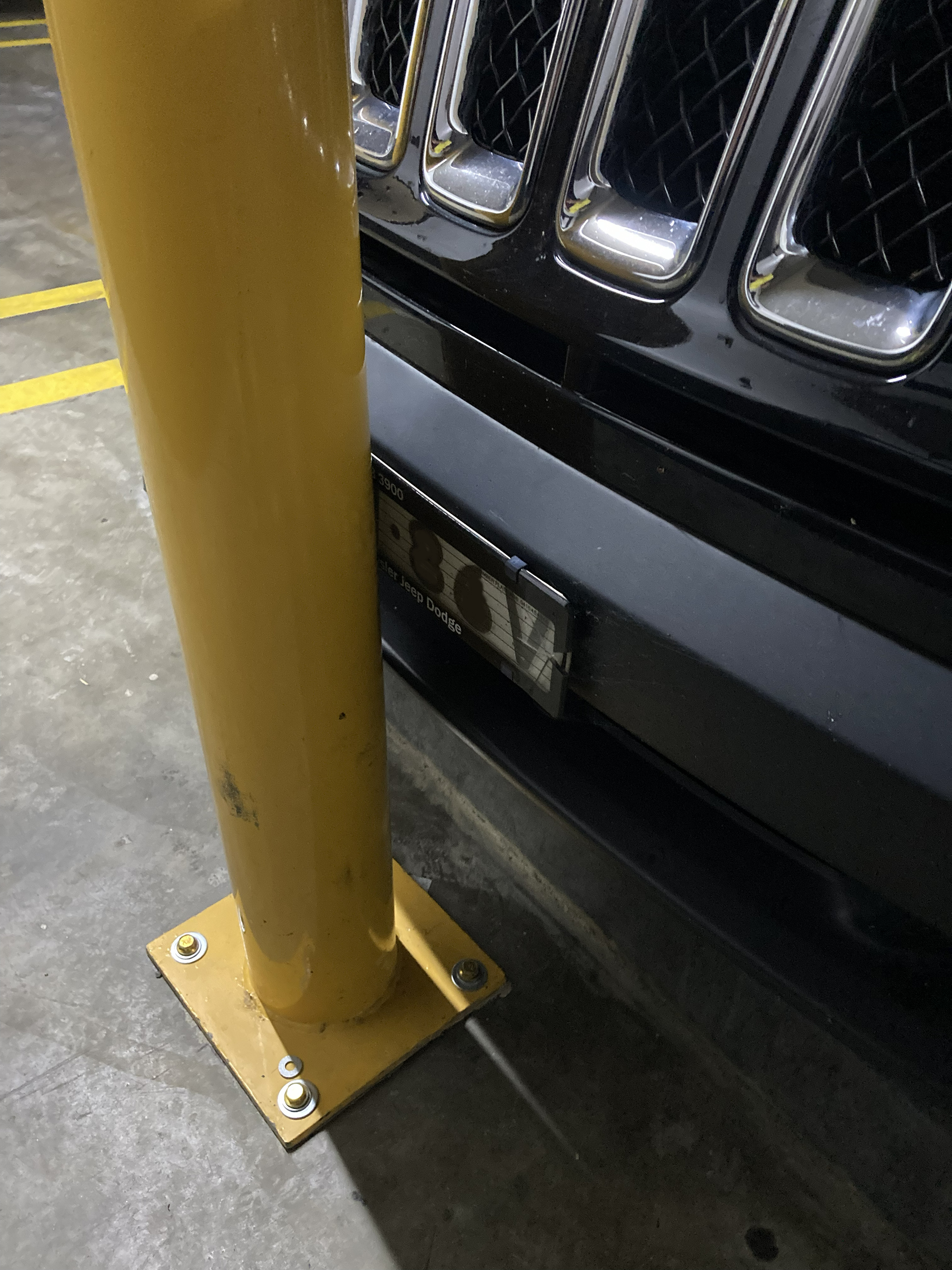 Steel bollard bent after being struck by a vehicle in a commercial building car park.